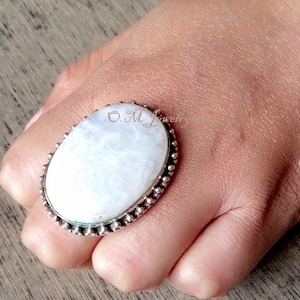 May include: A silver ring with a large oval white moonstone. The ring has a beaded edge.