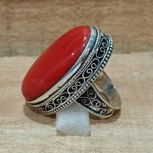 May include: A silver ring with an oval-shaped red gemstone set in a decorative silver band.