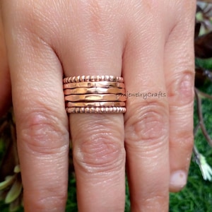 May include: A set of five rose gold stacking rings. The rings are made of hammered metal and have a textured finish. The rings are worn on a finger.