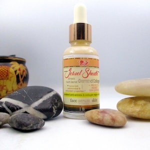 May include: A clear glass bottle with a gold cap and a label that reads "Jeruel Sheath Aince's Youth Secret Diamond Collagen". The bottle is sitting on a white surface with several smooth stones.