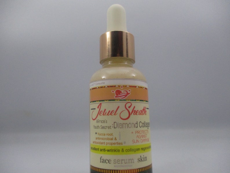 May include: A glass bottle of face serum with a gold cap and a label that reads "Jeruel Sheath Africa's Youth Secret: Diamond Collage". The label also lists the ingredients "Yucca root, antimicrobial & antioxidant properties" and "Protects against sun damage". The bottle is labeled "face serum skin".