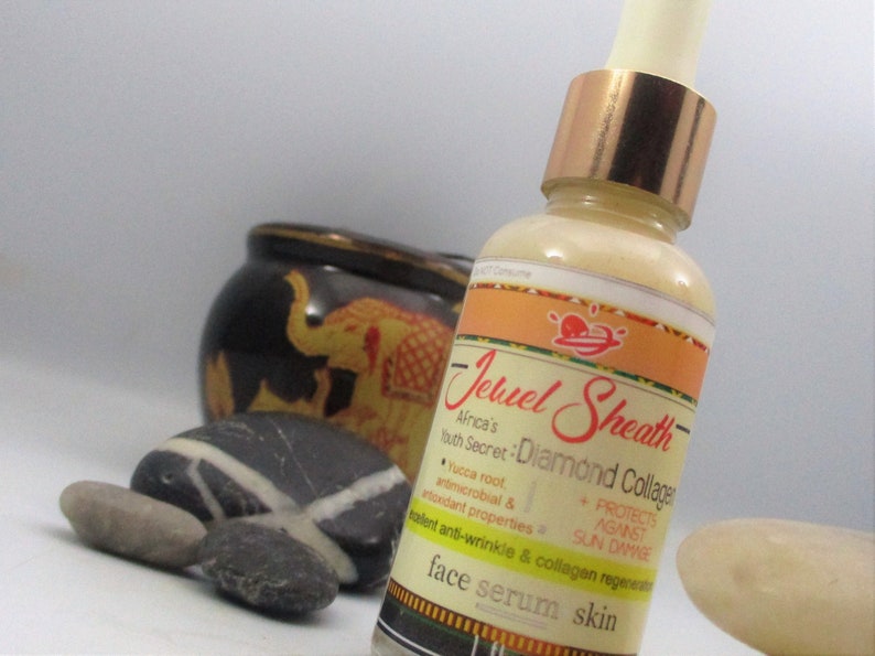 May include: A clear glass bottle with a gold lid and a label that reads "Jewel Sheath Africa's Youth Secret: Diamond Collagen". The label also includes the text "Yucca root, antimicrobial & antioxidant properties, protects against sun damage, talent anti-wrinkle & collagen regeneration, face serum skin".