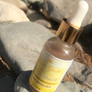 May include: A clear glass bottle with a gold cap and a white dropper. The bottle is filled with a light brown liquid. The label on the bottle reads "Golden Glow" and "Facial Sheath". It also says "It's a Vitamin A powerhouse" and "Botox for soft and supple skin". The bottle is labeled "Face Serum - Skin" and "1 fl oz".
