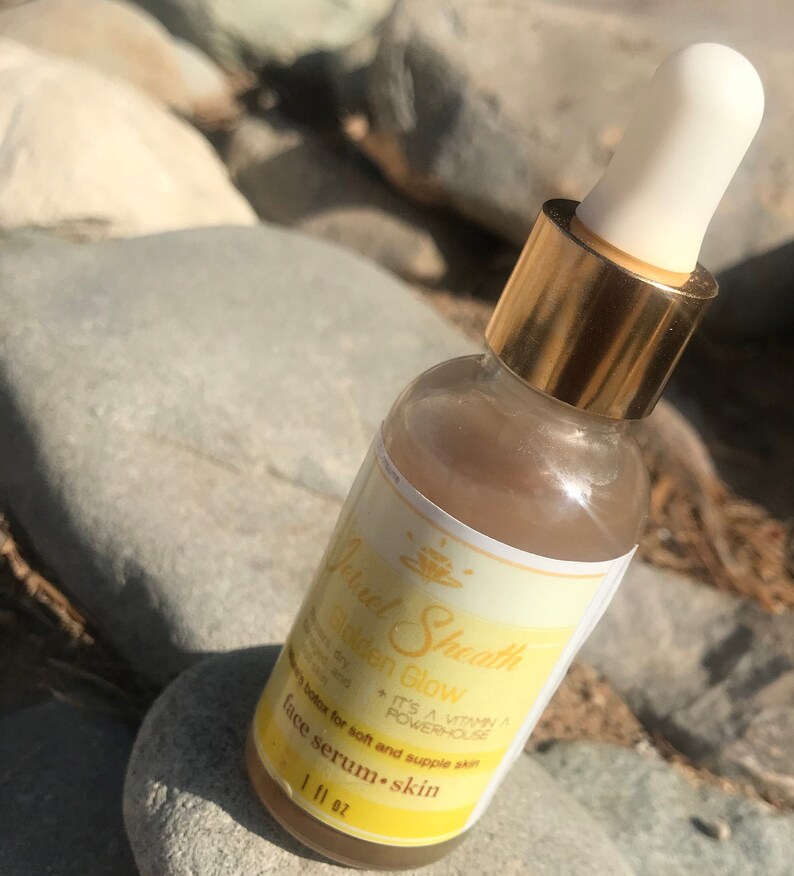 May include: A clear glass bottle with a gold cap and a white dropper. The bottle is filled with a light brown liquid. The label on the bottle reads "Golden Glow" and "Facial Sheath". It also says "It's a Vitamin A powerhouse" and "Botox for soft and supple skin". The bottle is labeled "Face Serum - Skin" and "1 fl oz".