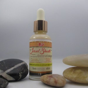 May include: A glass bottle of Jebuel Sheath Africa's Youth Secret Diamond Collagen face serum skin. The bottle has a gold cap and a dropper. The bottle is sitting on a table with some decorative stones.