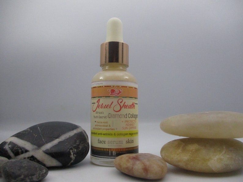 May include: A glass bottle of Jebuel Sheath Africa's Youth Secret Diamond Collagen face serum skin. The bottle has a gold cap and a dropper. The bottle is sitting on a table with some decorative stones.