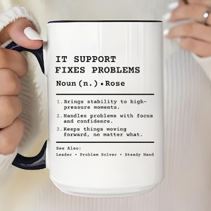 Puede incluir: Taza de cerámica blanca con interior y asa negros. La taza presenta el texto "IT SUPPORT FIXES PROBLEMS" con una definición. La definición incluye las palabras "estabilidad", "enfoque" y "confianza".