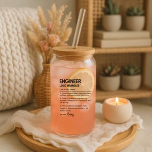 May include: A clear glass tumbler with a bamboo lid and a clear straw, filled with a pink beverage and a lemon slice. The tumbler has the text "ENGINEER LOGIC WRANGLER" printed on it. A candle and decorative items are in the background.