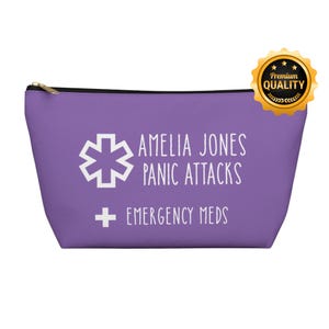 Pode incluir: Uma bolsa roxa com zíper e texto branco "AMELIA JONES PANIC ATTACKS EMERGENCY MEDS". Apresenta um símbolo médico branco e um selo dourado "Premium Quality".