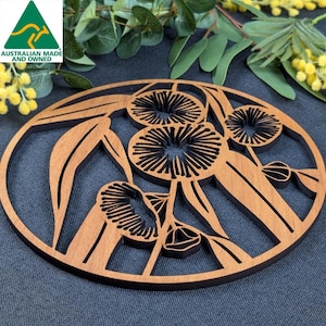 May include: Oval wooden coaster with a laser-cut floral design. The coaster has a dark brown border and a lighter brown interior with detailed cutouts of flowers and leaves. Made in Australia.