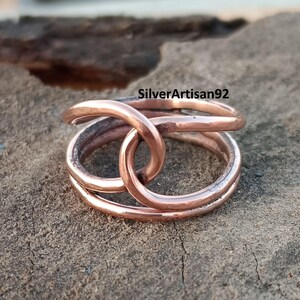 Puede incluir: Un anillo de cobre con un dise&ntilde;o de doble bucle. El anillo est&aacute; hecho de alambre grueso y tiene un acabado pulido.
