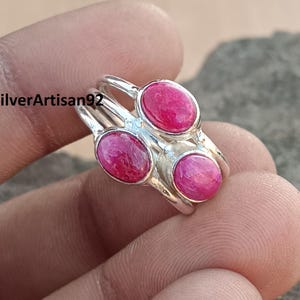 May include: A silver ring with three oval-shaped pink gemstones. The ring is made of sterling silver and features a delicate design.
