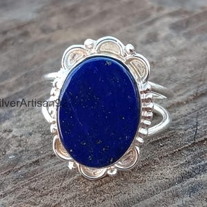 May include: A silver ring with a blue lapis lazuli stone set in an oval bezel. The ring has a decorative, scalloped edge.