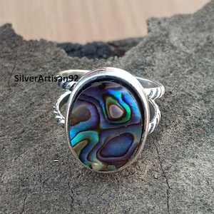 Könnte beinhalten: Ein Silberring mit einem blauen, grünen und violetten Abalone-Muscheleinlege. Der Ring hat ein gedrehtes Band.