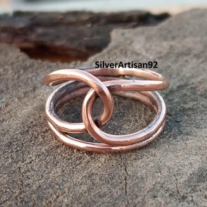 Puede incluir: Un anillo de cobre con un dise&ntilde;o trenzado. El anillo est&aacute; hecho de dos bandas de cobre que est&aacute;n entrelazadas. El anillo es un dise&ntilde;o simple y elegante.