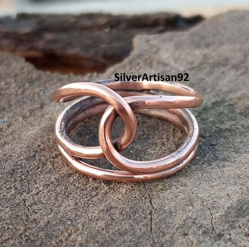 Puede incluir: Un anillo de cobre con un dise&ntilde;o trenzado. El anillo est&aacute; hecho de dos bandas de cobre que est&aacute;n entrelazadas. El anillo es un dise&ntilde;o simple y elegante.