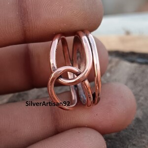 Puede incluir: Un anillo de cobre con un dise&ntilde;o anudado. El anillo est&aacute; hecho de tres hebras de alambre que se retuercen juntas para formar un nudo.