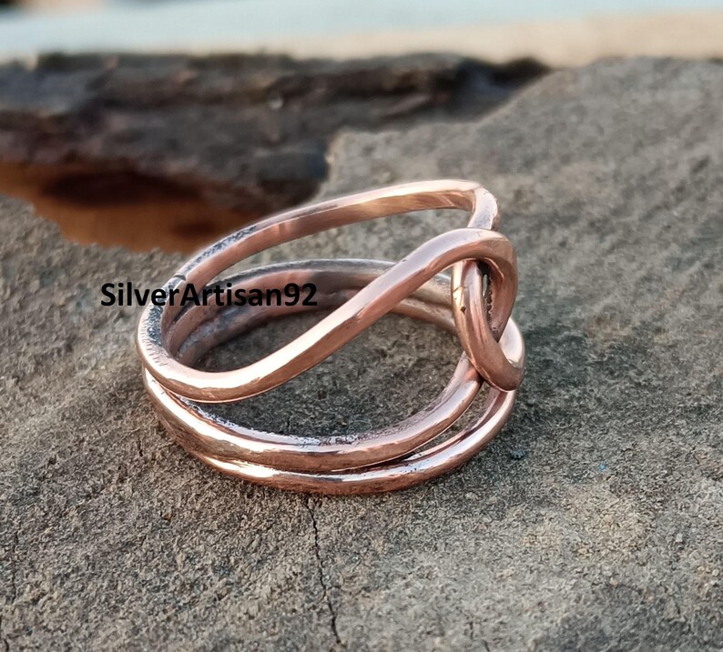 Puede incluir: Un anillo de cobre con un dise&ntilde;o trenzado. El anillo est&aacute; hecho de tres hilos de alambre que se trenzan para formar un nudo.
