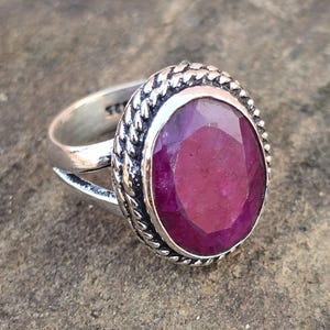 Puede incluir: Un anillo de plata con una gran piedra preciosa rosa facetada de forma ovalada engastada en un borde de cuerda.