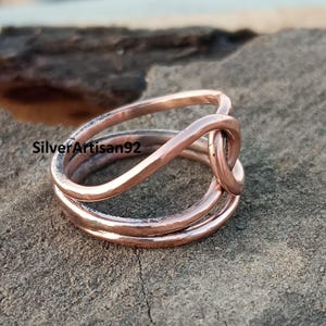 Puede incluir: Un anillo de cobre con un dise&ntilde;o trenzado. El anillo est&aacute; hecho de tres hilos de alambre que se trenzan juntos para formar un nudo.