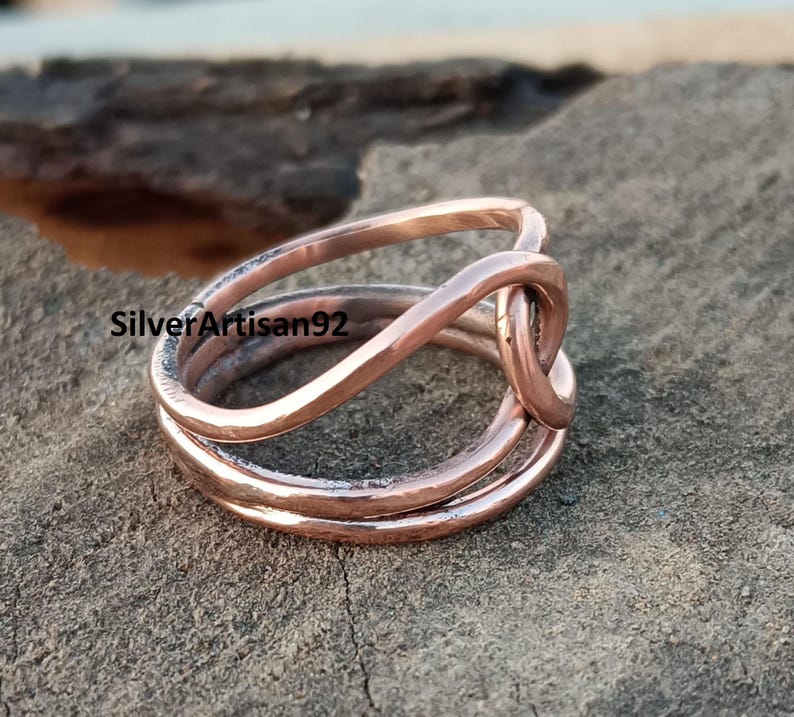 Puede incluir: Un anillo de cobre con un dise&ntilde;o trenzado. El anillo est&aacute; hecho de tres hilos de alambre que se trenzan juntos para formar un nudo.