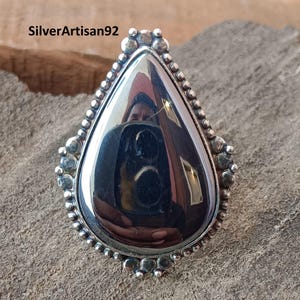 May include: A silver ring with a teardrop-shaped black gemstone. The ring has a beaded border.