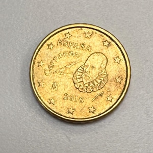 May include: A gold-coloured coin featuring a portrait of a man with a ruffled collar. The coin has the text "ESPAÑA Cervantes" and the year "2016" along with several stars. The coin is a Euro coin.