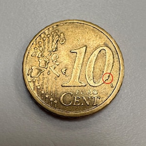 May include: A close-up of a gold-coloured 10 Euro cent coin. The coin features the number "10" prominently displayed, along with the words "Euro" and "Cent". The coin's design includes a map of Europe and stars.