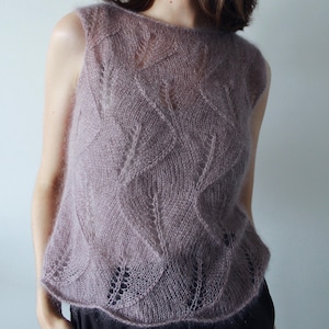 Könnte beinhalten: Ein ärmelloses Strickoberteil in staubigem Mauve mit einem zarten, durchbrochenen Blattmuster im gesamten Stoff. Das Kleidungsstück ist aus einem weichen, flauschigen Garn mit einer transparenten, luftigen Textur, einem weiten Rundhalsausschnitt und einem geraden Saum gefertigt.