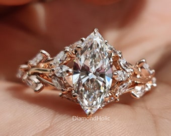 May include: A marquise-cut diamond ring with a rose gold band. The ring features a large central diamond and smaller accent diamonds. The band has a floral design. The ring is displayed on a person's hand.