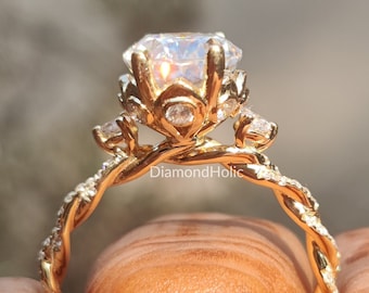 May include: A gold engagement ring with a large, clear gemstone at the centre. The ring features a twisted band and smaller accent stones. The ring is held between two fingers.