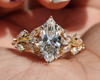 May include: A marquise-cut diamond engagement ring with a gold band. The ring features a large, clear marquise-cut diamond as the centerpiece, surrounded by smaller diamonds and intricate gold detailing. The ring is held in a hand with painted nails.