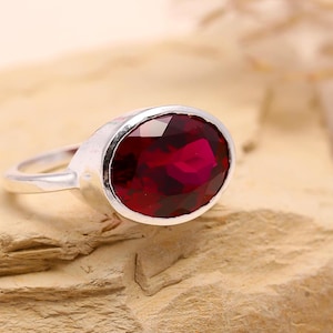 May include: A silver ring featuring a large, oval-shaped, deep red gemstone.