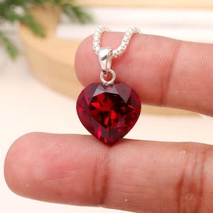 May include: A silver necklace featuring a heart-shaped, faceted, deep red pendant. The pendant is a vibrant gemstone. The chain is a delicate silver box chain. The pendant is suspended from a small silver bail.