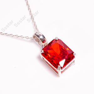 May include: A silver chain necklace with a pendant featuring a large, red, square-shaped gemstone.