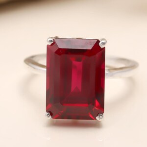 May include: A silver ring with a large, emerald-cut ruby gemstone.