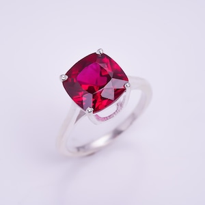 Può includere: Un anello d'argento con una grande pietra rossa di forma quadrata.