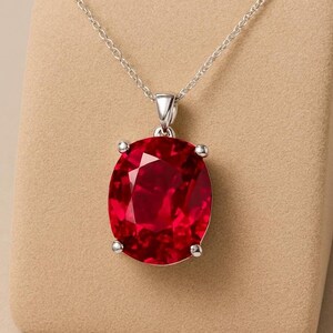 Può includere: Una collana d'argento con un grande pendente a forma di pietra preziosa rossa brillante a taglio ovale. La pietra preziosa è tenuta in posizione da quattro griffe d'argento e pende da una delicata catena d'argento. Il pendente è un gioiello suggestivo.