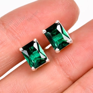 May include: A pair of silver earrings with emerald green square-shaped gemstones.