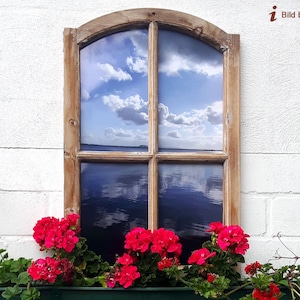May include: A rustic wooden window frame with a view of a blue sky and water. Bright red flowers in a green planter box sit below the window. A solar-powered lamp is to the left of the window.