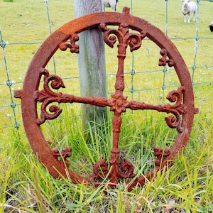 Könnte beinhalten: Ein rostiges Metallrad mit komplizierten Designs, vor dem Hintergrund von grünem Gras und einem Holzzaun.