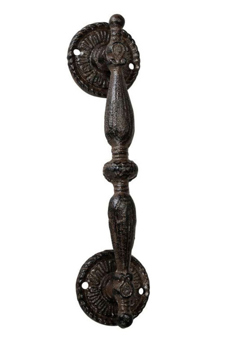 May include: A rustic, cast iron door pull with a dark brown finish. The handle has an ornate, vertical design with decorative circular backplates. The hardware is likely for a cabinet or door.
