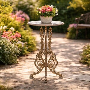 May include: A decorative, ornate, antique-style plant stand with a round top and intricate, golden-colored metalwork. A white pot filled with colorful flowers sits atop the stand, set in a garden setting.