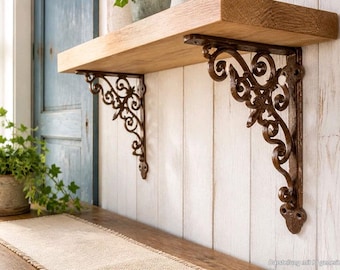 Puede incluir: Una repisa de madera de color claro natural sostenida por dos soportes de metal marrón oscuro con un diseño intrincado y ornamentado de volutas. Los soportes están montados contra una pared vertical de paneles blancos.