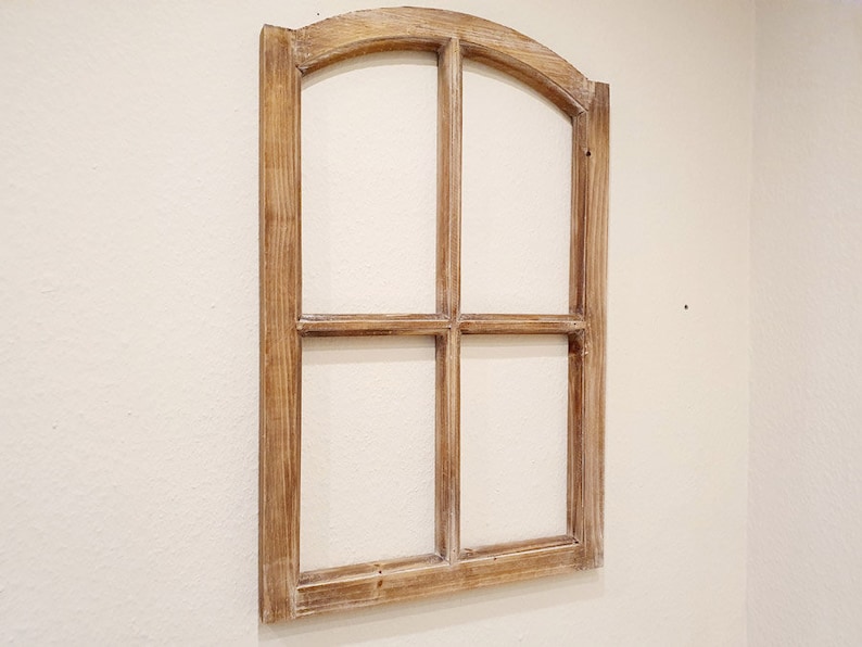 May include: A decorative wooden window frame with a light brown finish. The frame has an arched top and is divided into four panes. It is mounted on a cream-colored wall, adding a rustic touch to the decor.