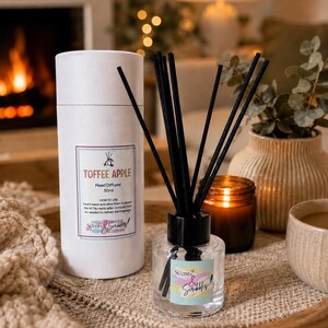 May include: A 50ml Toffee Apple reed diffuser in a clear glass bottle with black reeds, accompanied by a white cylindrical cardboard tube container. The label features the text Toffee Apple, instructions for use, and the Scents & Scribbles logo.