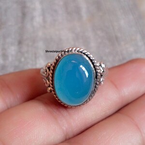Pode incluir: Anel de prata oval com uma pedra preciosa azul brilhante. O anel tem uma banda de prata detalhada e texturizada com um design de corda torcida em torno da pedra preciosa. O texto "ShreejaipurSilver97" é visível.