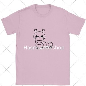 May include: A light pink t-shirt featuring a cute cartoon caterpillar with heart-shaped antennae. The caterpillar is drawn in black and has a smiling face. The text "Hasnaskittleshop" is printed below the caterpillar.