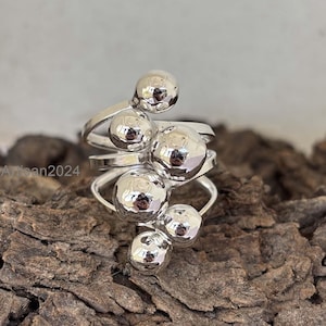 May include: A silver ring with a cluster of five round, textured spheres. The spheres are arranged in a cascading design, with the largest sphere at the top and the smallest sphere at the bottom.