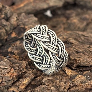 May include: A silver ring with a braided design. The ring is thick and has a wide band.